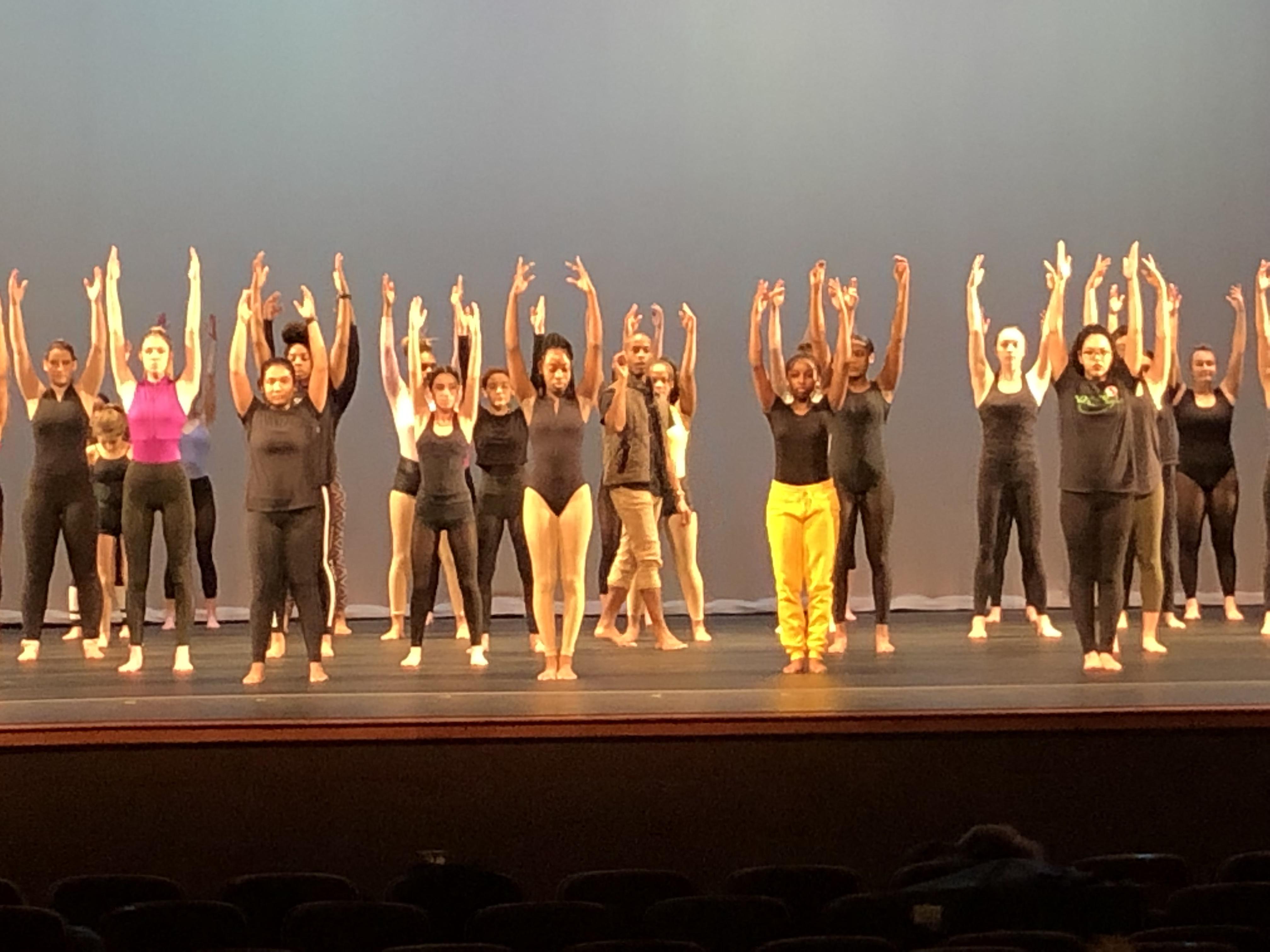 students on stage dancing with arms in the air